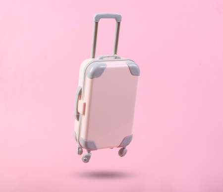 Mini travel luggage soaring on a pink background. Minimalism travel concept