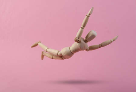 Falling down wooden puppet on pink background
