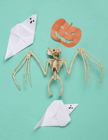 creative halloween layout. Vampire bat skeleton, origami ghosts, pumpkin on blue background. flat...