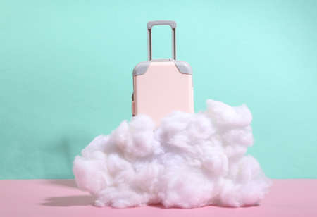 Toy luggage behind a fluffy cloud on blue pink pastel background. minimalism