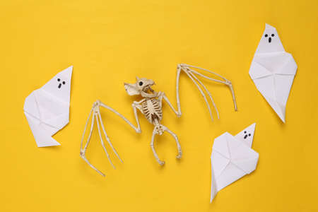 creative halloween layout. Vampire bat skeleton, origami ghosts on a yellow background. flat lay. top viewの写真素材