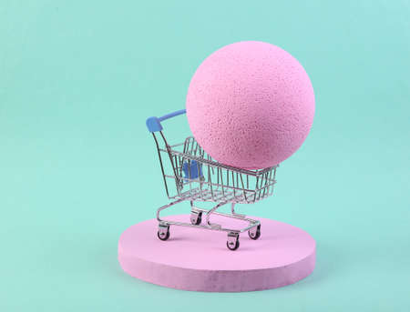 Minimalistic scene with shopping trolley and ball on blue background. Minimalism, creative shopping conceptの写真素材