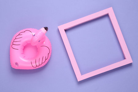 Inflatable flamingo and blank frame on a purple background. copy space