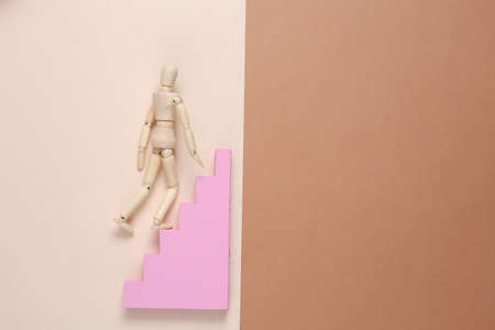 Puppet climbs up the stairs on brown beige background. Career growth concept, striving upの写真素材
