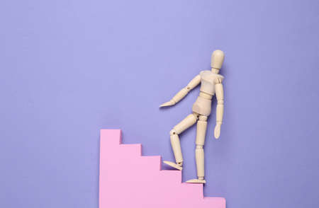 A puppet climbs up the stairs against a purple background. Career growth concept, striving upの写真素材