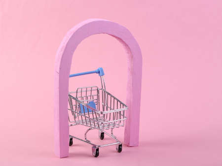 Minimalistic scene with an arch and a shopping trolley on a pink background. Minimalism, creative shopping conceptの写真素材