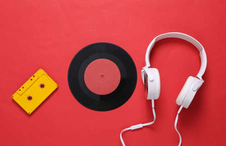 Stereo headphones with audio cassette, vinyl record on red background. Retro 80s still life. top...