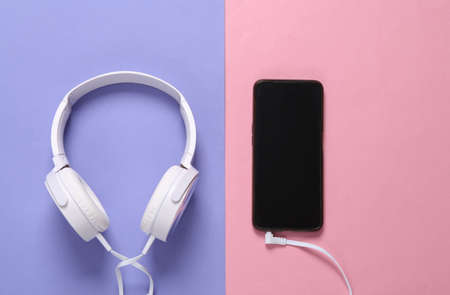 Stereo headphones connected to a smartphone on a purple-pink pastel backgroundの写真素材