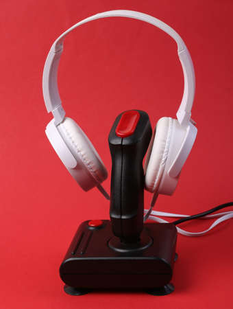 White stereo headphones with retro joystick on red background. gaming concept