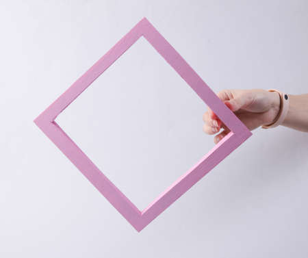 Female hand holds a pink frame on a gray background. fresh ideas, minimalism