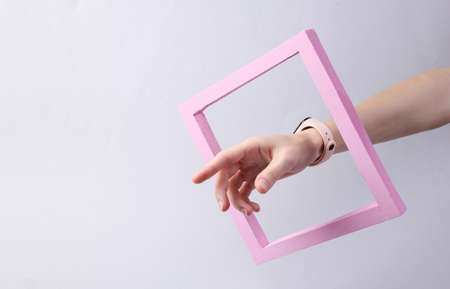 Female hand through a pink frame on a gray background. minimalism