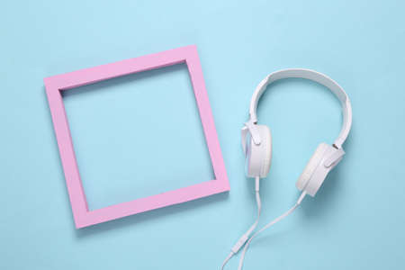White stereo headphones and pink blank frame on a light blue background. copy spaceの写真素材