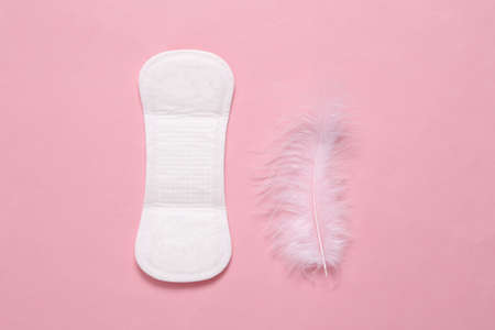 Feminine hygiene concept. Menstruation gynecological soft pad and feather on pink background