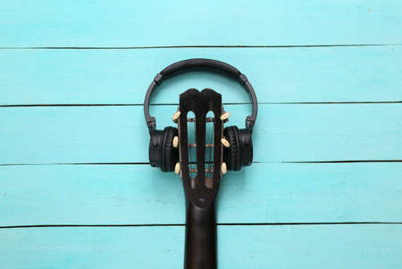 Acoustic guitar neck and headphones on blue wooden background. Online guitar lessons. musical concept. top view. flat layの写真素材