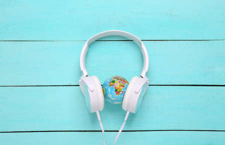 White stereo headphones with globe on blue wooden background. World Music Day. top view