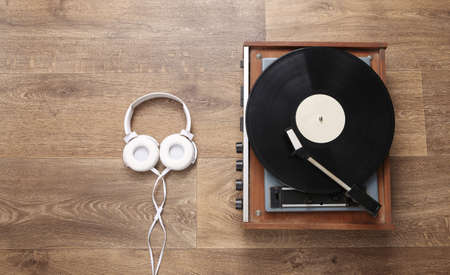 Stereo headphones and retro vinyl record player on wooden floor. musical concept. top view. flat layの写真素材