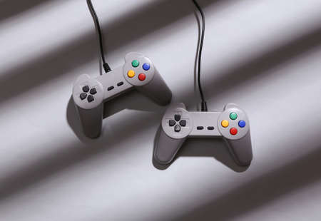 minimalistic layout. Retro gamepads with long striped trendy shadows on gray background. top view