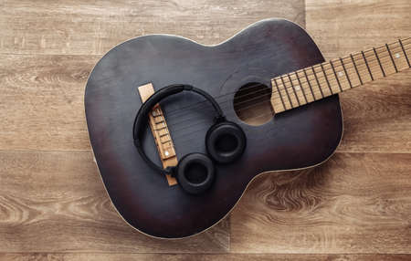 Acoustic guitar and headphones on wooden floor. Online guitar lessons. musical concept. top view....