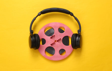 Pink retro audio reel with headphones on yellow background. Minimalism music concept. top view