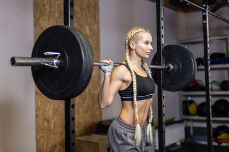 Portrait of sexy sport woman with barbell on shoulders in modern functional gymの写真素材