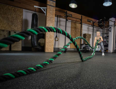 Athletic strong woman doing some exercises with battle rope in modern gym. functional training