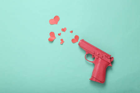 Love layout made with pink gun firing red heart on mint blue background. Creative valentines or...