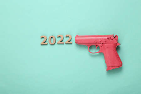 Pink pistol gun shooting 2022 on mint blue background. creative new year layout. flat lay. top viewの写真素材