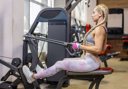 Young attractive woman in sportswear trains back muscles in exercise machine at gym