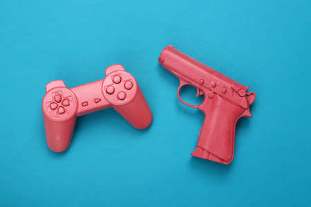 Gaming creative layout. Pink gamepad and pistol gun on a blue background. top view. flat lay