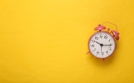 Pink alarm clock on yellow background. copyspace. top view. flat lay