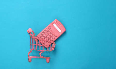 Mini pink supermarket trolley with calculator on blue background. top view. flat layの写真素材