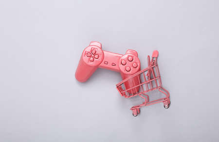 Mini pink supermarket trolley with gamepad on gray background. gaming concept. creative layout. top...