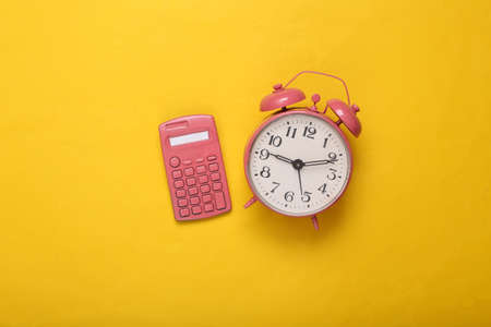 Pink calculator and alarm clock on yellow background. minimalism. creative layout. top view. flat layの写真素材