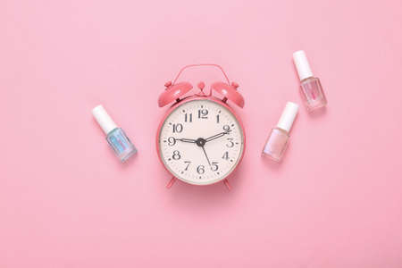 creative beauty layout. Alarm clock and bottles of nail polishes on a pink background. top view. flat layの写真素材