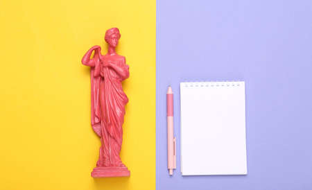 creative layout. Pink Antique greek goddess statue with notebook on purple yellow background....