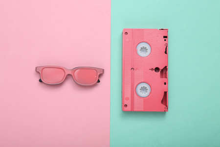 Pink video cassette and glasses on pink blue pastel background. minimalism. flat lay. top view.