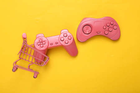 Pink shopping cart with joysticks on yellow background. top view. flat lay. minimalismの写真素材