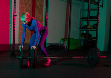 Fit woman collects barbell for workout in pink green neon gradient light at gym. Sport, fitness, lifestyle conceptの写真素材