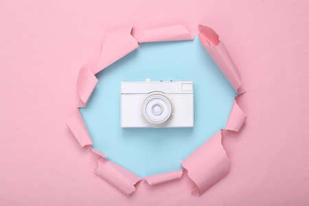 creative layout. White retro camera through torn hole of pink blue paper. Pastel color trend. fresh ideas. minimalism. concept art. flat lay. top view.の写真素材