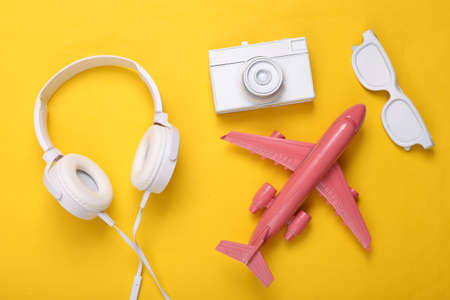creative travel layout. Toy air plane with White retro camera, glasses, and headphones on yellow...