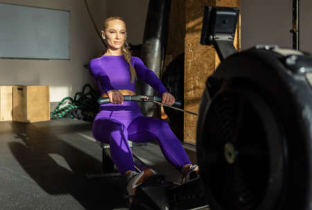 Woman doing cardio workout on rowing machine in the gym. Sportive girl works out in fitness club....