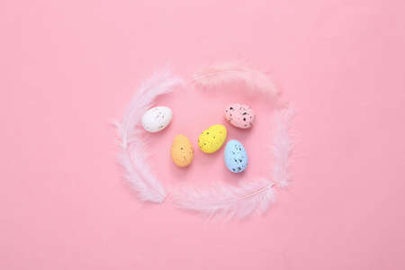 Easter composition of colored eggs and feathers on a pink background. top view. flat lay