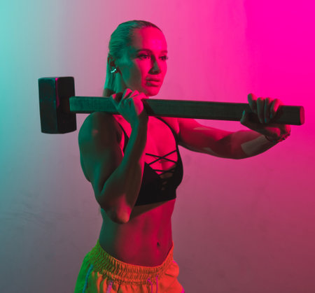 Fit woman with heavy sledgehammer for workout in pink green neon lighの写真素材