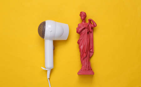 White hair dryer and antique statue on a yellow background. beauty concept. Hair care, hair style. top view. flat layの写真素材