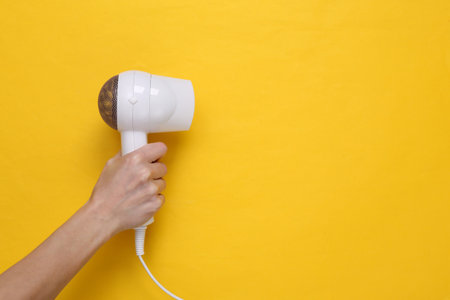 Hand holding White hair dryer on yellow background. beauty concept. Hair care, hair style. top view. flat lay. copy spaceの写真素材