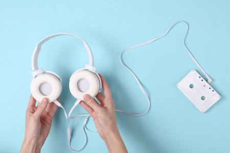 Female hands holding headphones and audio cassette on blue background. Music minimal concept