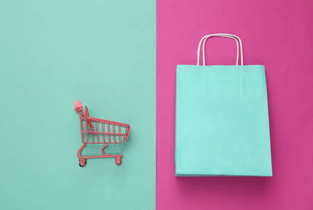 Mini shopping trolley and paper shopping package on pink blue background. top view. minimalismの写真素材