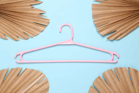 Plastic hanger on blue background with dry palm leaves. fashion layout. flat lay. top view
