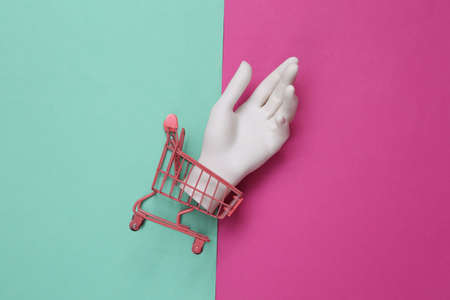 Shopping cart with mini dummy hand on blue-pink background. top view