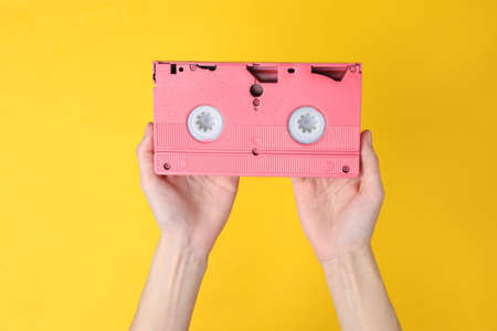 Hands holding retro video cassette on yellow backgroundの写真素材